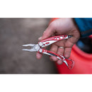 A hand holds a Leatherman Skeletool RX Multitool with pliers extended against a blurred outdoor background. This multitool features multiple functions and distinctive cut-out handle details.