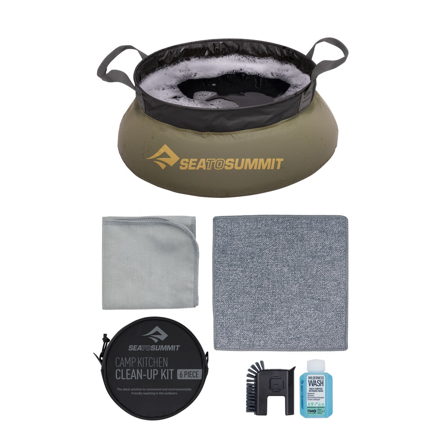 The Sea to Summit Camp Kitchen Clean Up Kit (6-Piece) includes a collapsible olive-green basin, two cloths, a small scrub brush, a bottle of biodegradable camp soap, and comes in a round carrying pouch labeled Camp Kitchen Clean-Up Kit 6 Piece—providing everything you need for convenient camping dishwashing in one handy kit.