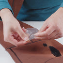 Person applying a clear substance to a brown wetsuit surface with a black stain.