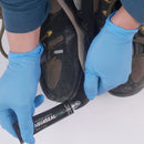Person applying Aquaseal SR to a black shoe with blue gloves on a white background