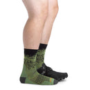 Side view of a person wearing black shoes and Darn Tough Mens Vert Micro Crew Ultra-Lightweight Socks, featuring a mountain pattern in green Merino wool. Only the legs from the knee down are visible against a white background.