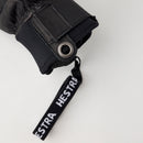 A close-up of the Hestra Men’s Fall Line Glove in black, featuring a metal grommet and a black strap with “HESTRA” in white lettering, set against a light background—an essential item in the Hestra Alpine Pro skiing glove collection.