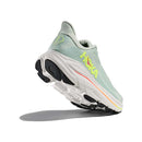 The Womens Clifton 10 Wide Running Shoe by Hoka is shown from a low rear angle in light green with yellow and orange accents, featuring a thick white sole and black tread, set against a white background.