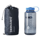A dark gray Therm-a-Rest NeoAir XLite NXT sleeping pad in a storage sack next to a clear gray plastic water bottle with measurement markings.