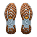 Two brown and light blue rubber shoe soles featuring a rugged, zigzag tread pattern and a yellow Vibram logo near the arch are displayed on a white background—these are the soles of the Hoka Womens Transport 2 sneakers, designed as sustainable city-to-trail running shoes for urban adventures and outdoor explorations.