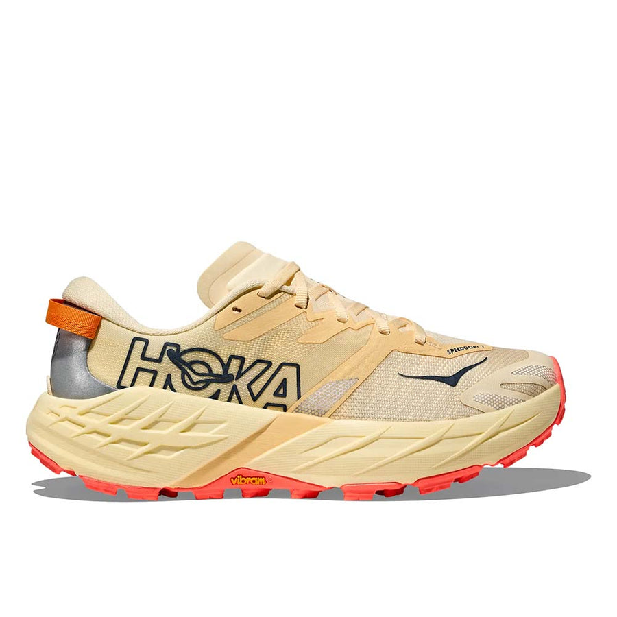 The Hoka Womens Speedgoat 7 Trail Running Shoe features a beige upper with black and orange accents, a chunky light yellow sole with orange tread, HOKA side branding, and a reflective heel detail—ideal for Hoka running shoe fans.