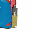 A close-up of a blue and pink Cotopaxi Allpa Mini 20L Travel Pack - Del Día backpack with a yellow side pocket holding a gray water bottle featuring a white llama graphic.