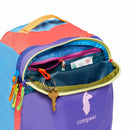 A vibrant Cotopaxi Allpa Mini 20L Travel Pack - Del Día, shown with its top pocket open to display keys on a keyring, mesh pouches, and various small items inside. The suitcase-style backpack features a purple colorway accented by contrasting zippers and is finished with a white Cotopaxi llama logo.