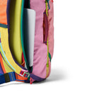 A close-up of the Cotopaxi Allpa 28L Travel Pack - Del Día shows its vibrant pink, yellow, green, orange, and blue panels. A silver laptop is partially visible inside the main compartment of this sustainable backpack. The background is white.