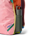 A close-up of the Cotopaxi Allpa 28L Travel Pack - Del Día, a sustainable backpack featuring vibrant pink, orange, red, and green colors with “Allpa 28” written on it and a gray water bottle in its side pocket.