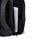 A silver laptop is partially tucked into a side zipper pocket of the Cotopaxi Allpa 35L Travel Pack, with the bag’s shoulder strap and recycled-fabric padding clearly visible against a white background.