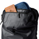 A Cotopaxi Allpa 35L Travel Pack in black, made from recycled fabrics, featuring a blue case and a partially visible brown passport holder in the front pocket.