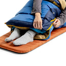A person in gray socks unzips the bottom of a Sea to Summit Circuit Down Sleeping Bag (-1°C) while lying on an orange sleeping pad.