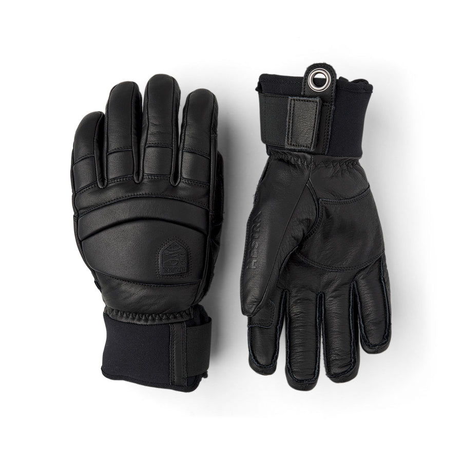 A pair of black insulated winter gloves, such as the Hestra Men’s Fall Line Glove, featuring reinforcement on the knuckles and wrist straps, displayed flat with one glove palm up and the other palm down on a white background—ideal cold weather skiing gloves.