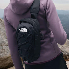 Person wearing a black The North Face sling bag with a scenic mountain background