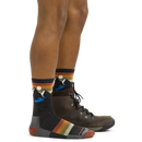 A person wearing brown hiking boots and Darn Tough Mens Sunset Ridge Micro Crew Lightweight Hiking Socks with a mountain, sun, and lake design. Only the lower legs are visible against a plain white background.