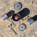 MSR Titan Kettle 900mL set, featuring two gray cups with lids, two metal sporks, and a red fuel canister stored inside the kettle—all arranged on a rocky outdoor surface—makes an ideal backpacking cookware solution.