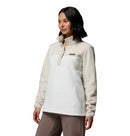 A woman wears the Columbia Womens Benton Springs™ Half Snap Pullover in cream and white with brown pants. She stands against a plain white background, looking slightly to the side with a neutral expression, showcasing casual comfort.