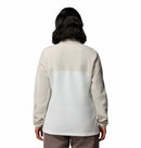 A woman with shoulder-length dark hair is seen from behind wearing the Columbia Womens Benton Springs™ Half Snap Pullover in off-white and white, paired with taupe pants, against a plain white background.