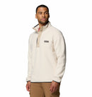 A man with short hair and a trimmed beard stands against a white background, wearing the Columbia Mens Helvetia Half Snap Fleece in cream, featuring a button collar and chest pocket. He looks slightly to his right.