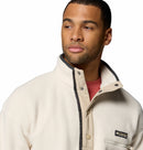 A man with short hair and a trimmed beard wears a cream Mens Helvetia Half Snap Fleece from Columbia, featuring a high collar, snap buttons, and the Columbia logo on the chest over a red shirt. He looks slightly to the side.