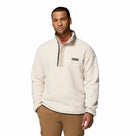 A man in the Columbia Mens Helvetia Half Snap Fleece, a cream-colored Sherpa with a high collar and snap buttons, paired with brown cargo pants, stands against a white background in cozy retro style.