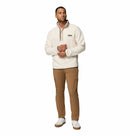 A man stands against a white background wearing the Columbia Mens Helvetia Half Snap Fleece, styled with brown cargo pants and white sneakers. He looks slightly to the side, his left hand touching his collar and right by his side.