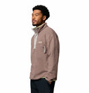 A man wearing the Columbia Mens Helvetia Half Snap Fleece in light brown stands against a plain white background, looking to the side with a neutral expression.