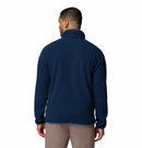 A man faces away from the camera, wearing a Columbia Mens Helvetia Half Snap Fleece in navy blue and light brown pants, set against a plain white background.
