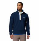 A man wears the Columbia Mens Helvetia Half Snap Fleece in navy blue, featuring a high collar, buttoned placket, and a zippered chest pocket. He stands looking slightly to the side.