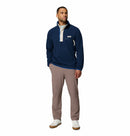 A man faces forward in a Columbia Mens Helvetia Half Snap Fleece—navy blue with a beige placket—paired with light brown pants and white sneakers. He has short hair, a slight beard, and his hands in his pockets against a white background.