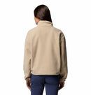 A person with long brown hair, seen from behind, wears the Columbia Womens Helvetia II Cropped Sherpa Half Snap Fleece in light beige and dark blue pants against a plain white background.