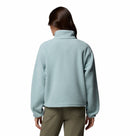 A person with long brown hair, seen from behind, wears the Columbia Womens Helvetia II Cropped Sherpa Half Snap Fleece in light blue and olive green pants, standing against a plain white background.