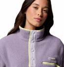 A woman with long dark hair wears the Columbia Womens Helvetia II Cropped Sherpa Half Snap Fleece in light purple with yellow trim and snap buttons, looking neutrally at the camera against a white background.