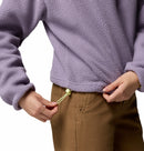 A person wearing the Columbia Womens Helvetia II Cropped Sherpa Half Snap Fleece in light purple with brown pants is adjusting the fleece’s drawstring hem. The persons face is not visible.