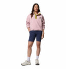 A woman faces forward against a plain white background wearing the Columbia Womens Helvetia II Cropped Sherpa Half Snap Fleece in light pink, paired with blue shorts, white socks, and white sneakers.
