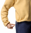 A person in blue pants adjusts the drawstring at the hem of the Columbia Womens Helvetia II Cropped Sherpa Half Snap Fleece, a PFAS-free water-repellent light yellow sweater.