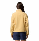 A person with long brown hair, seen from behind, wears the Columbia Womens Helvetia II Cropped Sherpa Half Snap Fleece in light yellow and dark blue shorts against a plain white background.