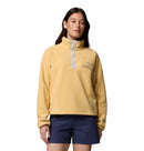 A woman wears the Columbia Womens Helvetia II Cropped Sherpa Half Snap Fleece in light yellow with a high collar and button placket, paired with navy blue shorts, standing against a white background.