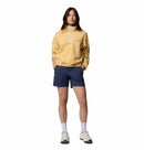 A woman stands with hands in her shorts pockets, wearing the Columbia Womens Helvetia II Cropped Sherpa Half Snap Fleece in light yellow, navy blue shorts, white socks, and white sneakers against a plain white background.