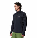 A man in a black Columbia Mens Crystal Leaf Omni-Heat Helix Technical Half Zip Fleece and green pants stands against a white background—an ideal technical midlayer for cool conditions.