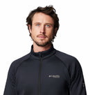 A man with short brown hair and a beard wears a black Columbia Mens Crystal Leaf Omni-Heat Helix Technical Half Zip Fleece and looks at the camera against a white background.