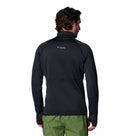 A man with dark hair, seen from behind, wears a black Columbia Mens Crystal Leaf Omni-Heat Helix Technical Half Zip Fleece and green pants against a plain white background.