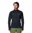 A man in a black Columbia Mens Crystal Leaf Omni-Heat Helix Technical Half Zip Fleece and green pants stands facing forward against a white background.