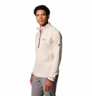 A man in a light beige Columbia Mens Crystal Leaf Omni-Heat Helix Technical Half Zip Fleece with a sleeve badge, paired with gray pants, stands against a white background.