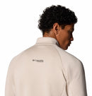 A person with short, curly hair is shown from the back wearing a light beige Columbia Mens Crystal Leaf Omni-Heat Helix Technical Half Zip Fleece. The Columbia logo is on the upper back against a white background.
