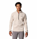 A young man with short curly hair wears a light beige Columbia Mens Crystal Leaf Omni-Heat Helix Technical Half Zip Fleece and gray pants, standing facing forward against a plain white background.