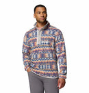 A man wears the Columbia Mens Helvetia II Printed Half Snap Fleece, featuring a vibrant print, high collar, and snap buttons, paired with gray pants against a plain white background.