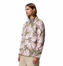 A man with long brown hair wears the Columbia Mens Helvetia II Printed Half Snap Fleece in light pink, green, and white with a chest pocket and beige pants, standing against a plain white background.