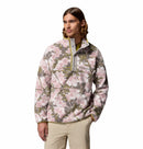 A man with long hair wears the Columbia Mens Helvetia II Printed Half Snap Fleece in pink, white, and green with a front zipper and chest pocket, paired with beige pants, standing against a plain white background.